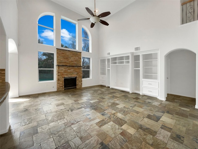 unfurnished living room with arched walkways, a fireplace, stone tile flooring, visible vents, and ceiling fan