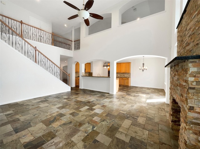 unfurnished living room with arched walkways, stairway, stone finish floor, baseboards, and ceiling fan with notable chandelier