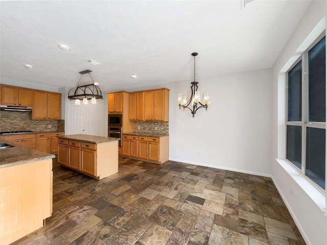 kitchen with backsplash, appliances with stainless steel finishes, stone finish floor, a kitchen island, and baseboards