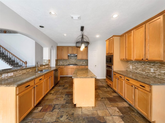 kitchen featuring stone tile floors, stainless steel appliances, a sink, visible vents, and a center island