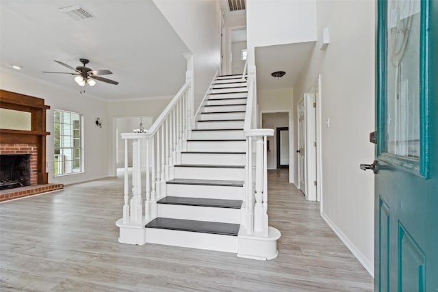 foyer featuring visible vents, stairway, crown molding, a brick fireplace, and ceiling fan