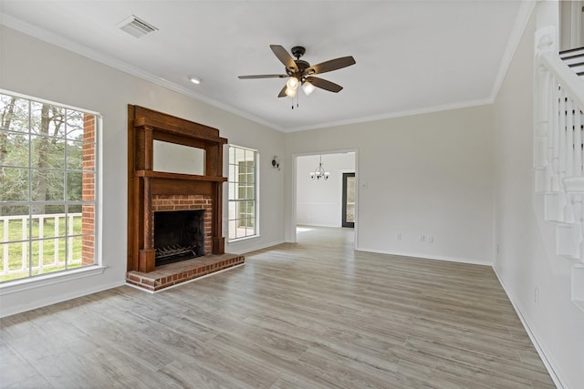 unfurnished living room featuring light wood finished floors, visible vents, a brick fireplace, crown molding, and ceiling fan with notable chandelier