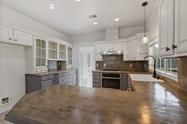 kitchen featuring open shelves, a sink, under cabinet range hood, stainless steel oven, and tasteful backsplash