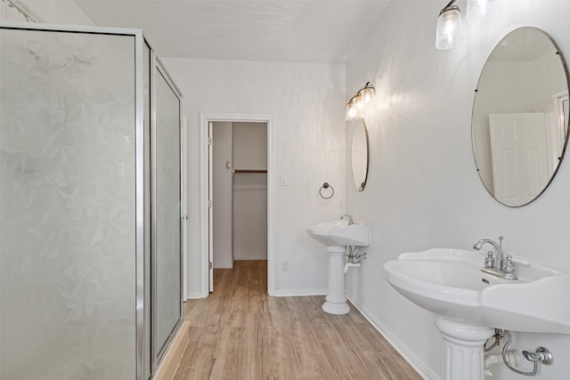 bathroom featuring a spacious closet, a shower stall, baseboards, and wood finished floors