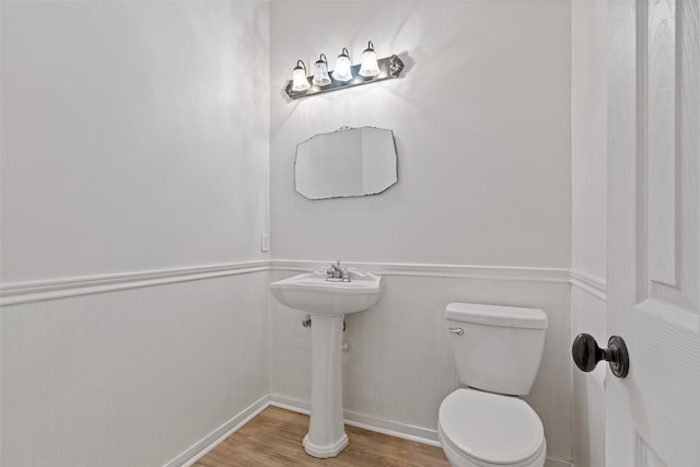 half bathroom with wainscoting, toilet, and wood finished floors