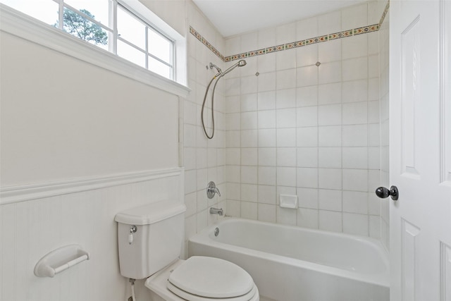 bathroom featuring toilet, tub / shower combination, and a wainscoted wall