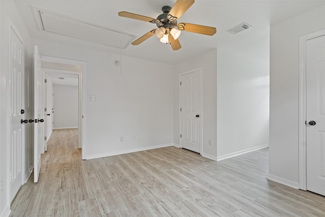 empty room with visible vents, baseboards, light wood finished floors, attic access, and ceiling fan