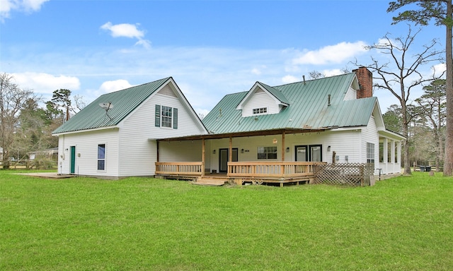 rear view of house featuring a deck, a lawn, a chimney, and metal roof