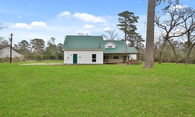 rear view of property featuring fence, a lawn, and metal roof