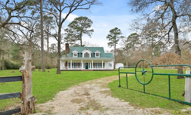 view of front of home featuring a front yard, driveway, a porch, a chimney, and metal roof