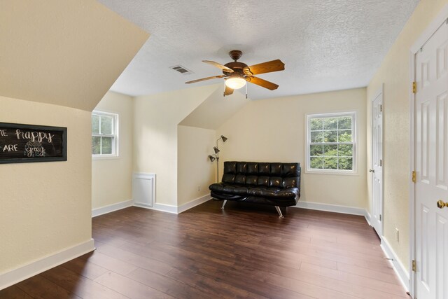 living area with visible vents, a textured ceiling, wood finished floors, baseboards, and ceiling fan