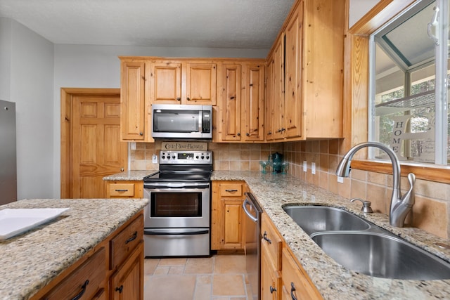 kitchen with decorative backsplash, light stone counters, appliances with stainless steel finishes, and a sink