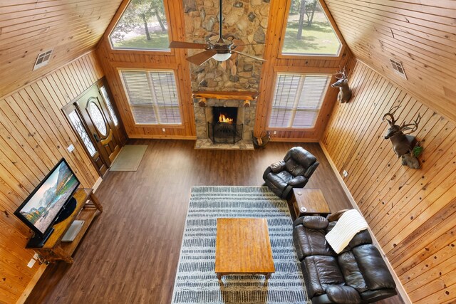 unfurnished living room featuring wooden walls, a stone fireplace, wood finished floors, plenty of natural light, and high vaulted ceiling