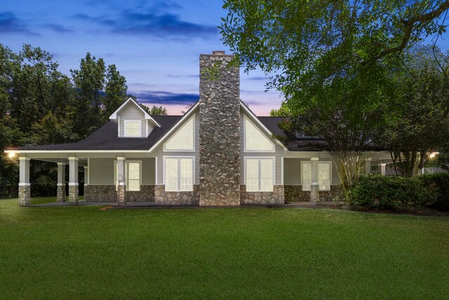rear view of house with a yard, stone siding, a porch, and a chimney