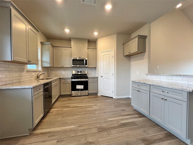 kitchen featuring stainless steel appliances, backsplash, gray cabinetry, a sink, and light wood-type flooring