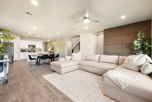 living area with recessed lighting, visible vents, light wood finished floors, and stairs