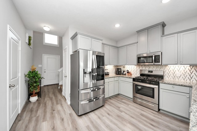 kitchen with light stone counters, light wood finished floors, stainless steel appliances, decorative backsplash, and gray cabinetry