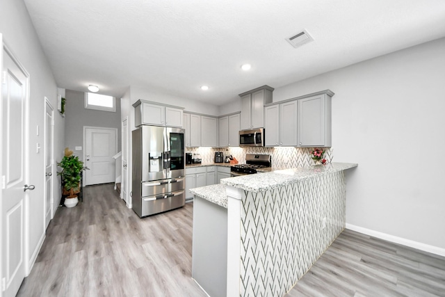 kitchen featuring stainless steel appliances, visible vents, decorative backsplash, gray cabinetry, and a peninsula