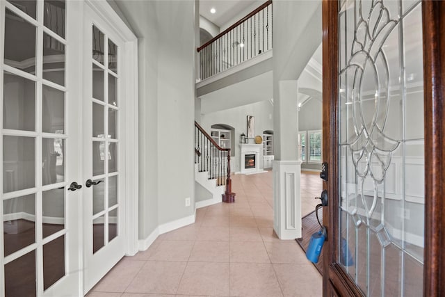 tiled foyer entrance featuring arched walkways, french doors, stairway, a high ceiling, and a warm lit fireplace