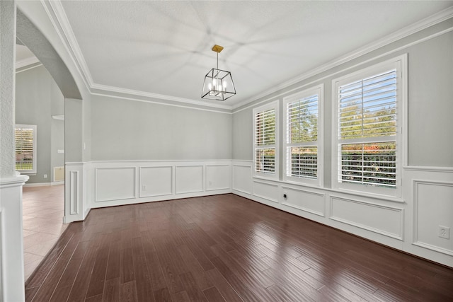 unfurnished dining area with crown molding, a decorative wall, wood finished floors, and an inviting chandelier