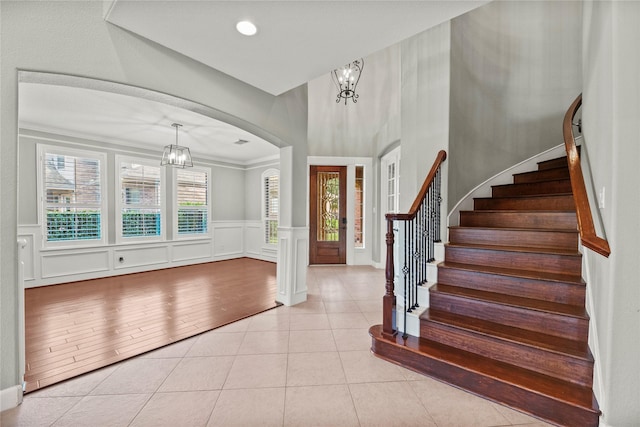 foyer with stairs, light tile patterned floors, a decorative wall, and an inviting chandelier