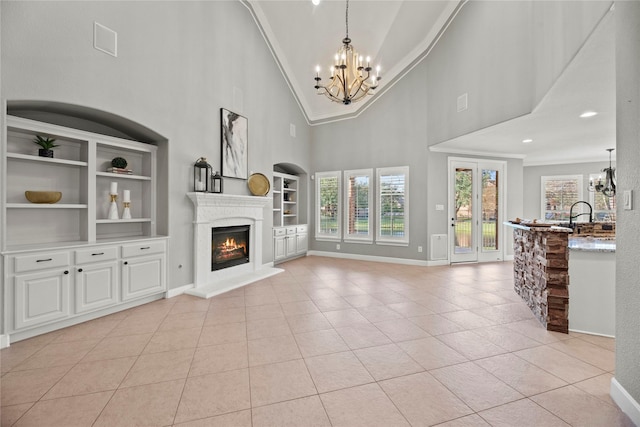 unfurnished living room with a chandelier, a warm lit fireplace, light tile patterned floors, built in shelves, and ornamental molding