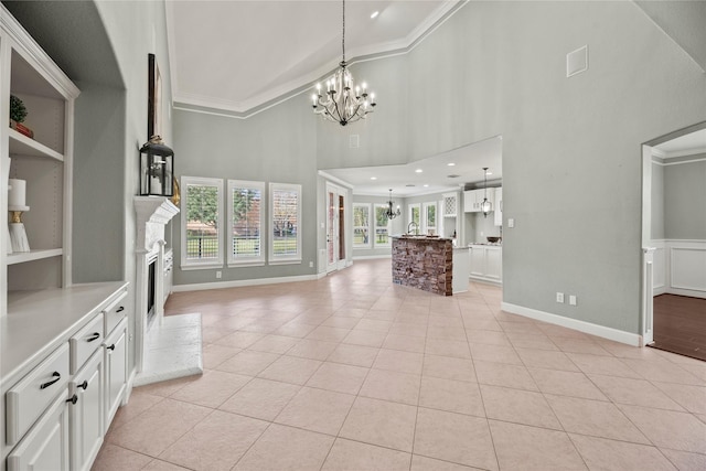 unfurnished living room featuring light tile patterned floors, a fireplace with raised hearth, a towering ceiling, crown molding, and a chandelier