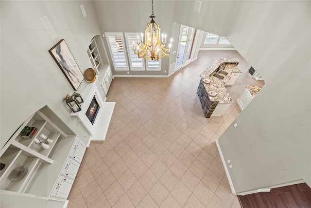 interior space with light tile patterned floors, a high ceiling, baseboards, a glass covered fireplace, and an inviting chandelier