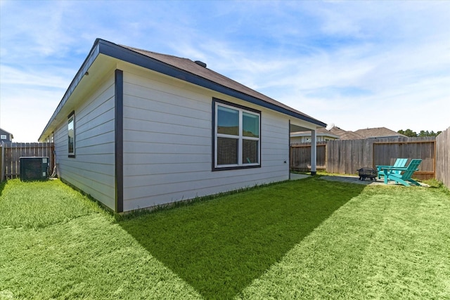 rear view of house with central AC unit, a lawn, a fenced backyard, and an outdoor fire pit