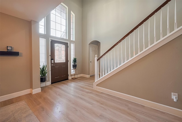 entryway with baseboards, arched walkways, stairway, wood finished floors, and a high ceiling