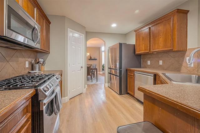 kitchen featuring stainless steel appliances, arched walkways, brown cabinetry, and a sink