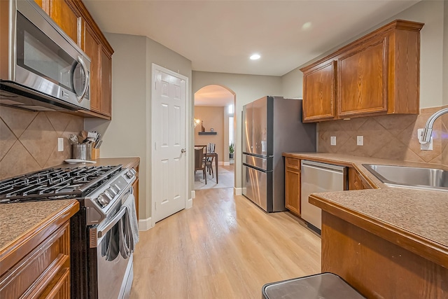 9314 Dune Gate Ct, Humble, TX 77396 - kitchen featuring appliances with stainless steel finishes, arched walkways, light wood-style flooring, brown cabinetry, and recessed lighting