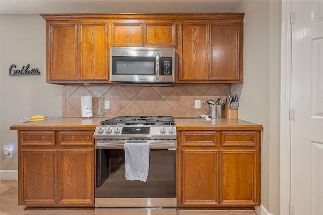 kitchen with brown cabinetry, appliances with stainless steel finishes, light countertops, and decorative backsplash