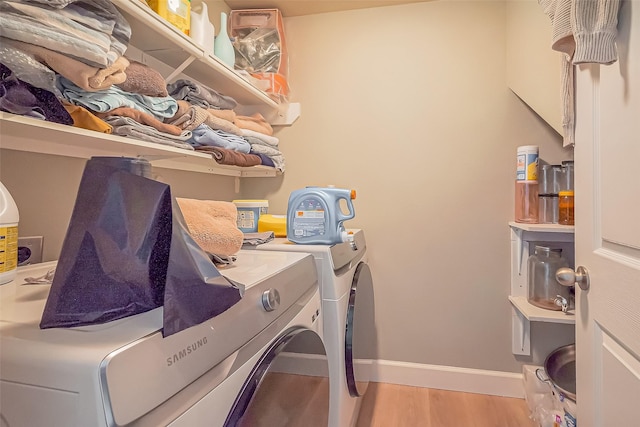 clothes washing area featuring laundry area, separate washer and dryer, wood finished floors, and baseboards