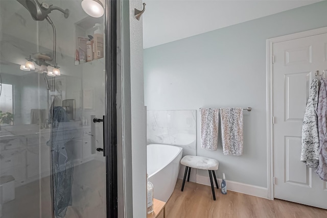 full bathroom featuring a freestanding bath, a shower stall, baseboards, and wood finished floors