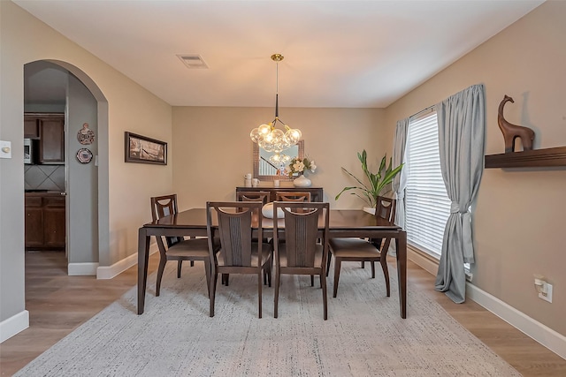 dining space featuring a chandelier, arched walkways, wood finished floors, and visible vents