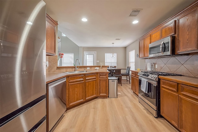 9314 Dune Gate Ct, Humble, TX 77396 - kitchen featuring appliances with stainless steel finishes, light wood-type flooring, decorative backsplash, a peninsula, and brown cabinetry