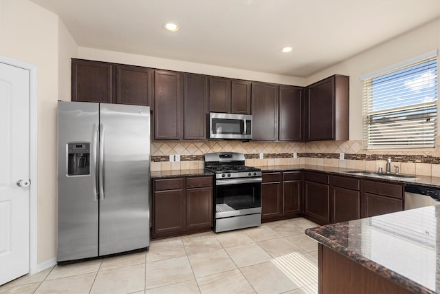 kitchen featuring dark brown cabinets, appliances with stainless steel finishes, dark stone countertops, and a sink