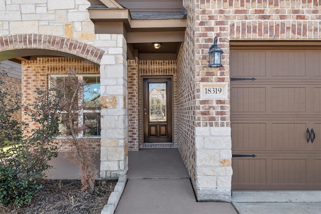 doorway to property with a garage, stone siding, and brick siding