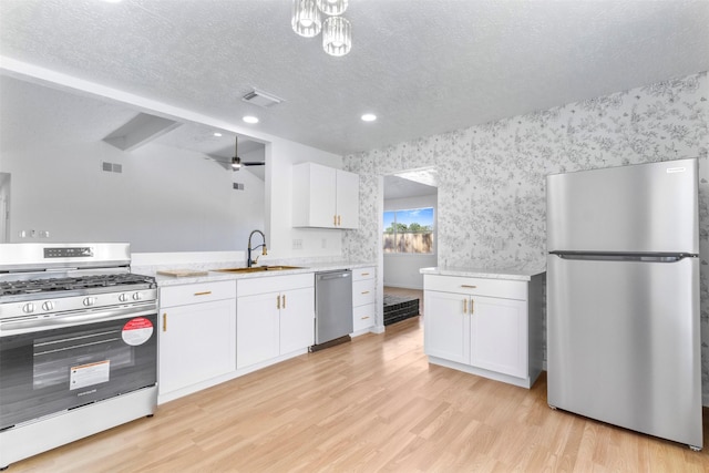 kitchen with wallpapered walls, stainless steel appliances, a textured ceiling, light wood-style floors, and a sink