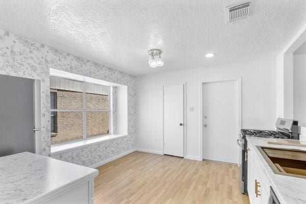 kitchen with visible vents, white cabinets, stainless steel gas range, light countertops, and light wood-type flooring