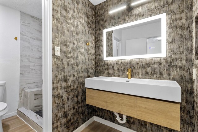 bathroom with toilet, walk in shower, wood finished floors, and vanity