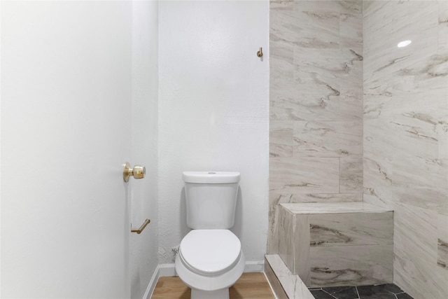 bathroom featuring a tile shower, toilet, and baseboards