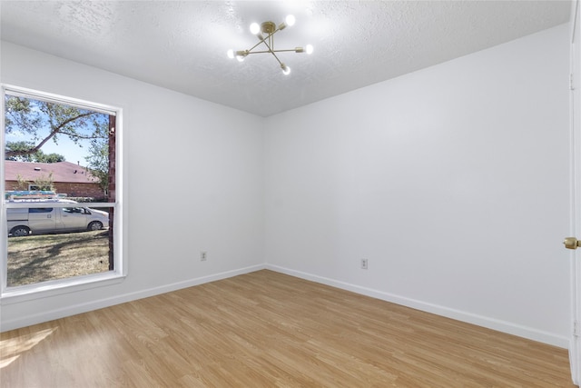 empty room with a textured ceiling, light wood finished floors, baseboards, and a notable chandelier