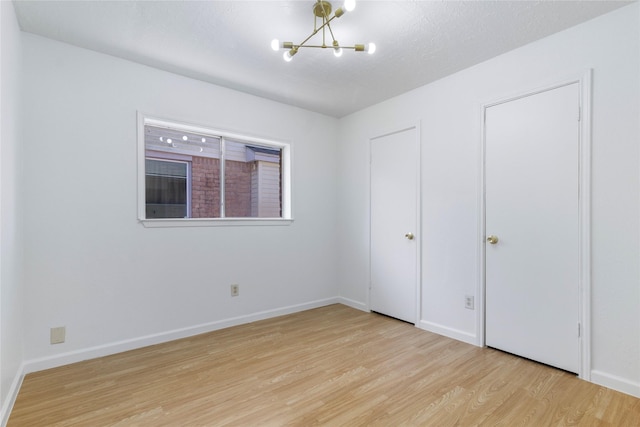 unfurnished bedroom with a notable chandelier, baseboards, and wood finished floors