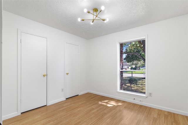 unfurnished bedroom featuring light wood-style floors, a notable chandelier, a textured ceiling, and baseboards