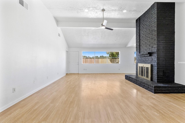 unfurnished living room featuring a textured ceiling, lofted ceiling, wood finished floors, a ceiling fan, and a brick fireplace