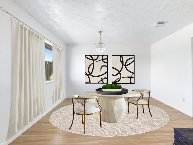 dining area with visible vents, a textured ceiling, an inviting chandelier, and wood finished floors