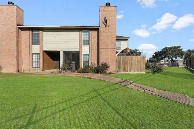 rear view of house with brick siding, fence, a chimney, and a lawn