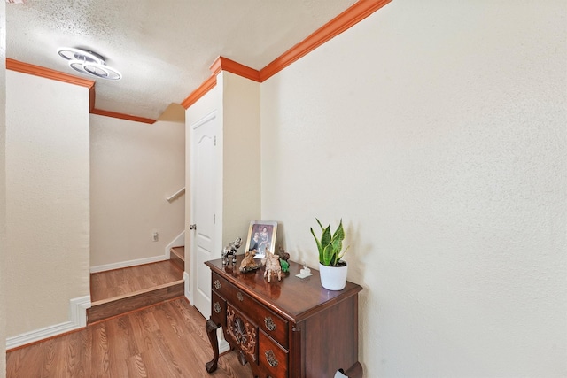 hall with a textured ceiling, wood finished floors, baseboards, stairs, and ornamental molding